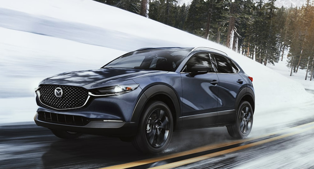A blue 2023 Mazda CX-30 subcompact SUV is driving on a wet road.