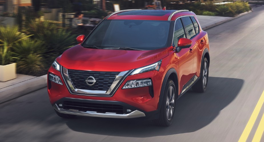 A red 2023 Nissan Rogue small SUV is driving on the road. 