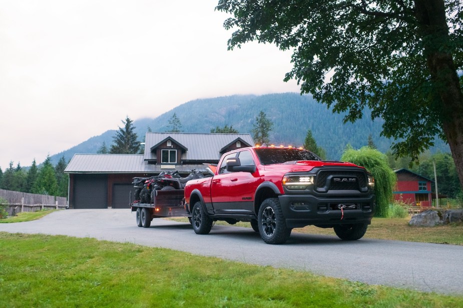 Red heavy duty Ram 2500 towing a trailer down a driveway, a mountain visible in the background.