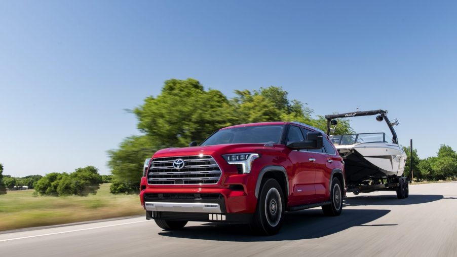 Red Toyota Sequoia SUV showing off its higher towing capacity than the entry-level Jeep Wagoneer Series I by pulling a boat down a country road.