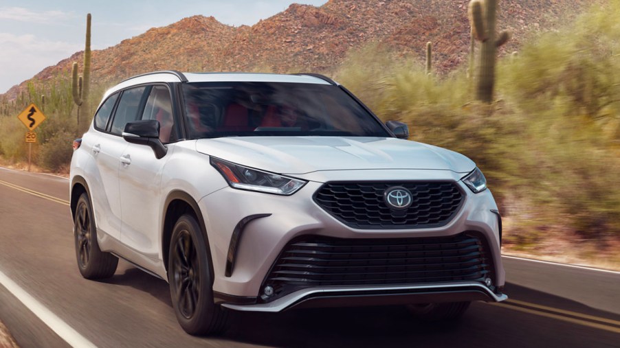 A white 2023 Toyota Highlander is driving on the road.
