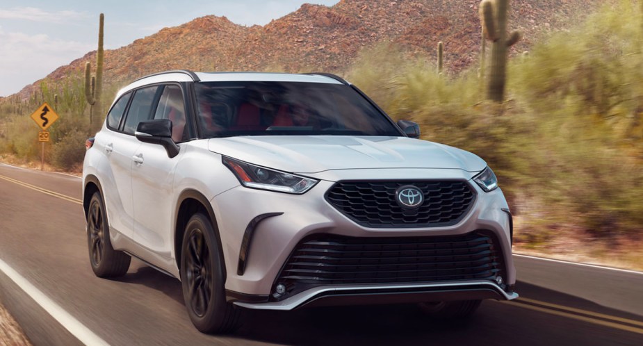 A white 2023 Toyota Highlander is driving on the road.