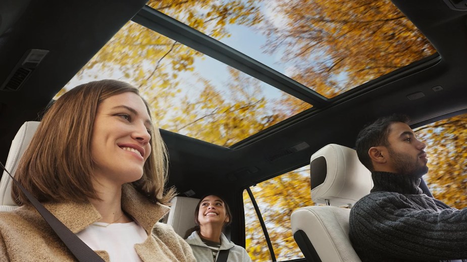 A family drives through a forest, orange fall leaves visible through their hybrid SUV's glass sunroof.