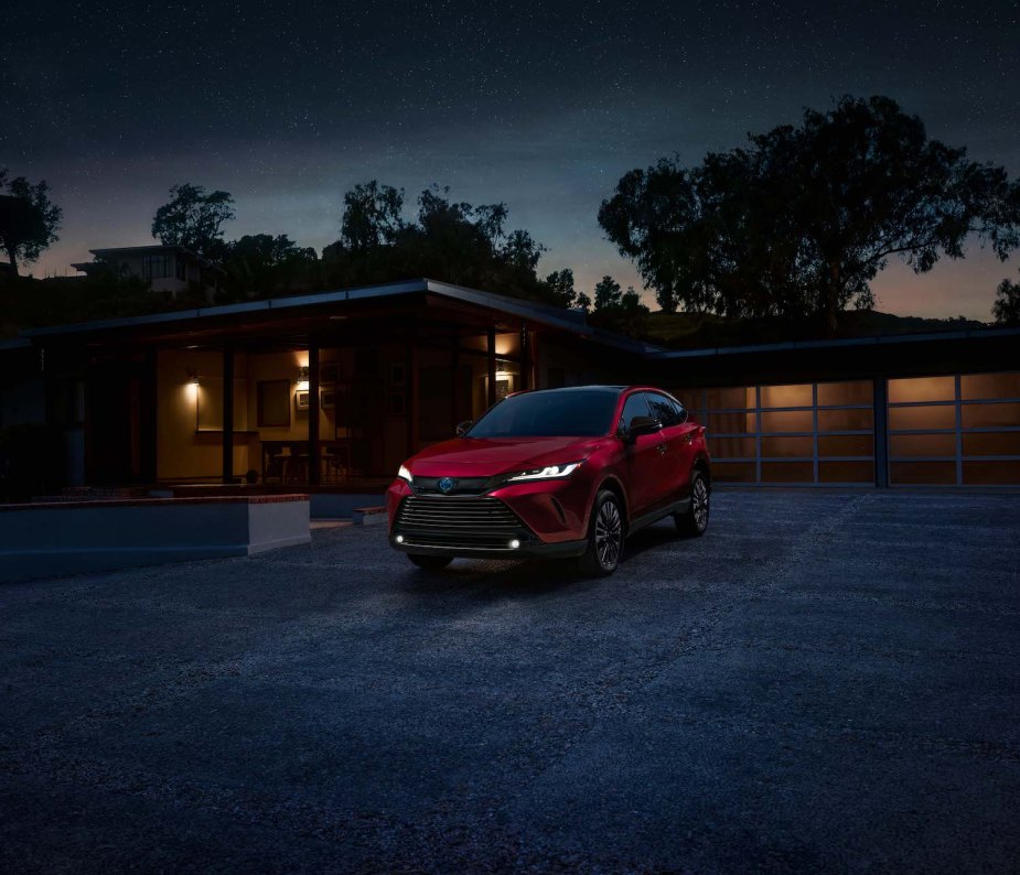 Red Toyota Venza hybrid crossover car parked in front of a house at night for a promo photo, a starry sky visible in the background.
