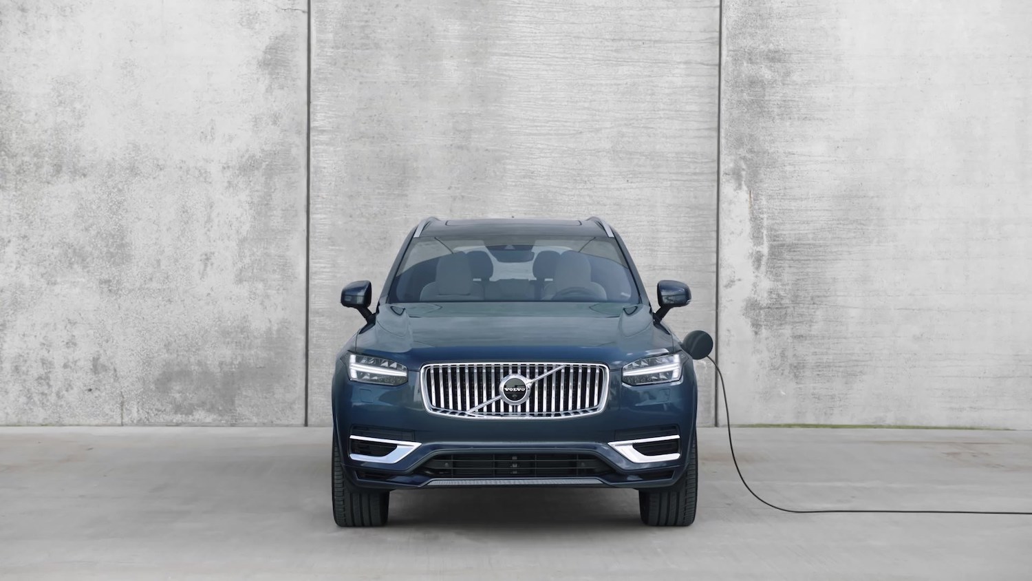 Volvo plug-in hybrid crossover SUV parked in front of a concrete wall, a charging cable attached.