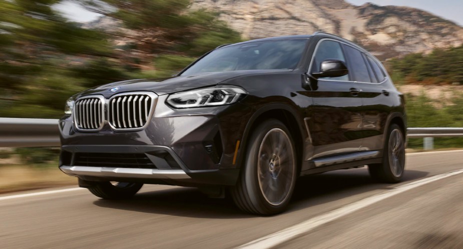 A gray 2023 BMW X3 small luxury SUV is driving on the road. 
