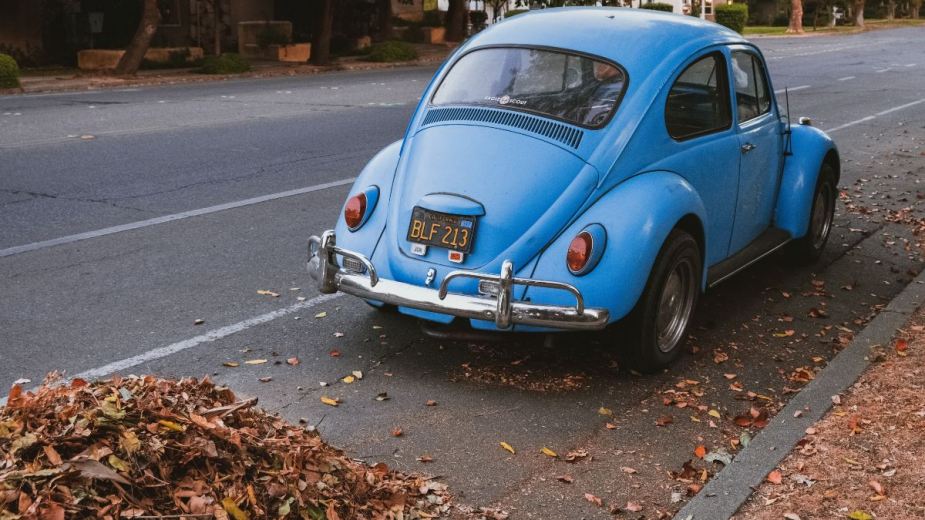 Blue VW Beetle near a leaf pile, highlighting how parking on leaves can make a car start on fire