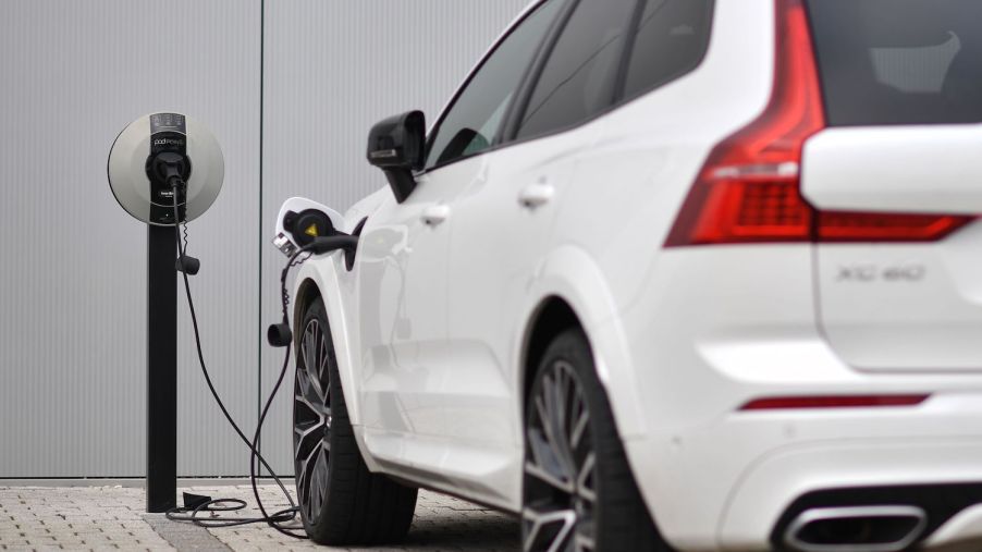 Closeup of a white Volvo plug-in hybrid charging its battery in front of a dealership.