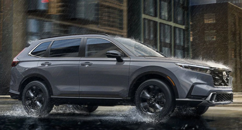 A gray 2023 Honda CR-V small SUV is driving on a damp road.