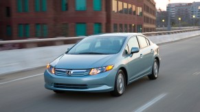 A silver Honda Civic Hybrid driving down a city street, the Honda Civic Hybrid is a fuel-efficient used hybrid sedan