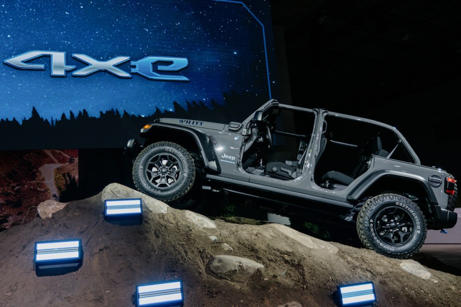 A grey Jeep Wrangler 4xe parked indoors on a fake rock. 