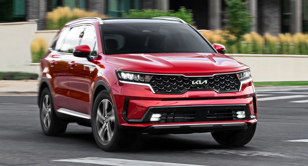 A red 2023 Kia Sorento Hybrid midsize hybrid SUV is driving on the road. 