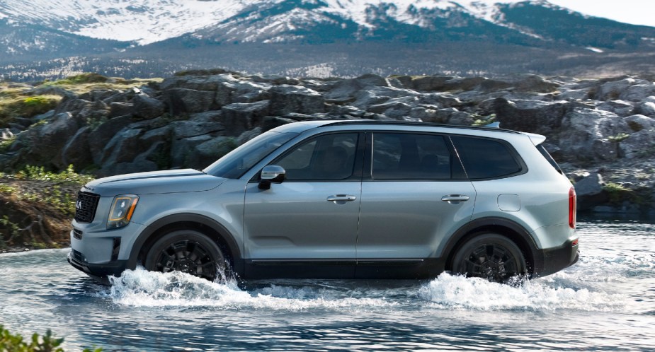 A gray Kia Telluride is driving in shallow water. 