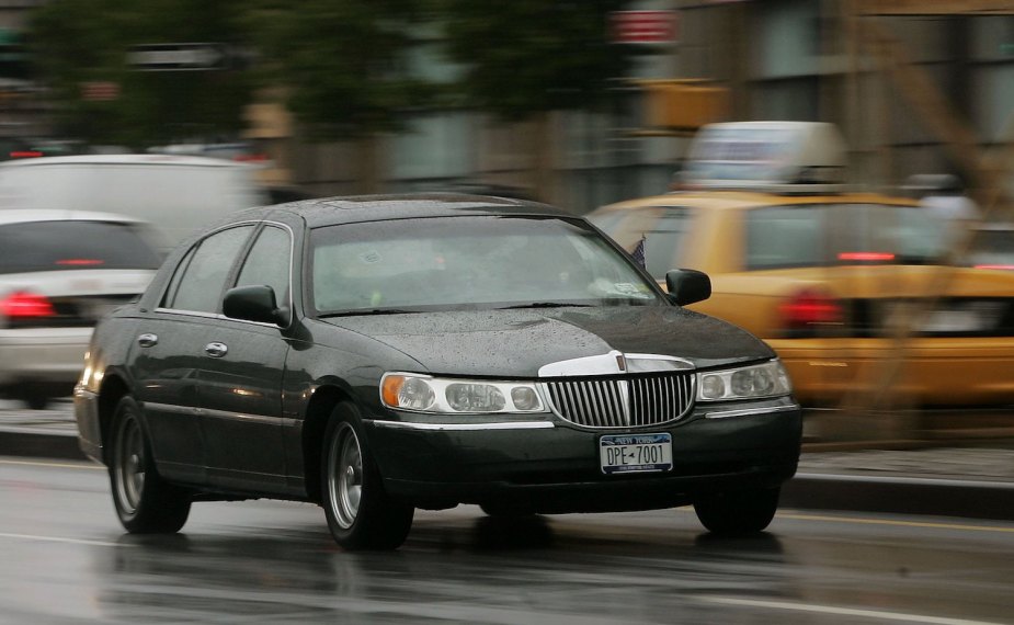 A black Lincoln Town Car speeds through New York City traffic with both a police and Ford taxi Crown Victoria visible in the background.