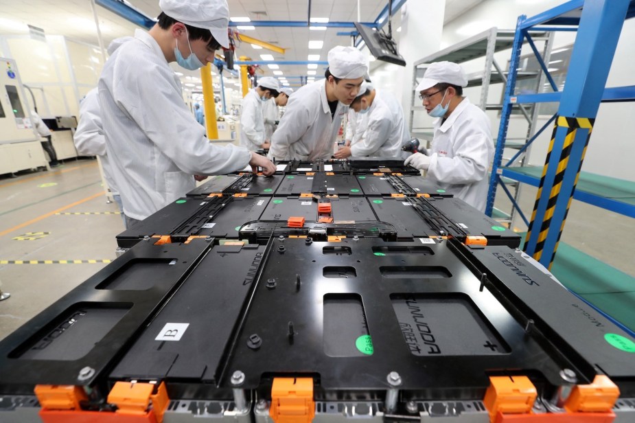 Closeup of assembled Lithium-ion cells at the Xinwangda Electric Vehicle Battery Co., uniformed workers visible in the background.