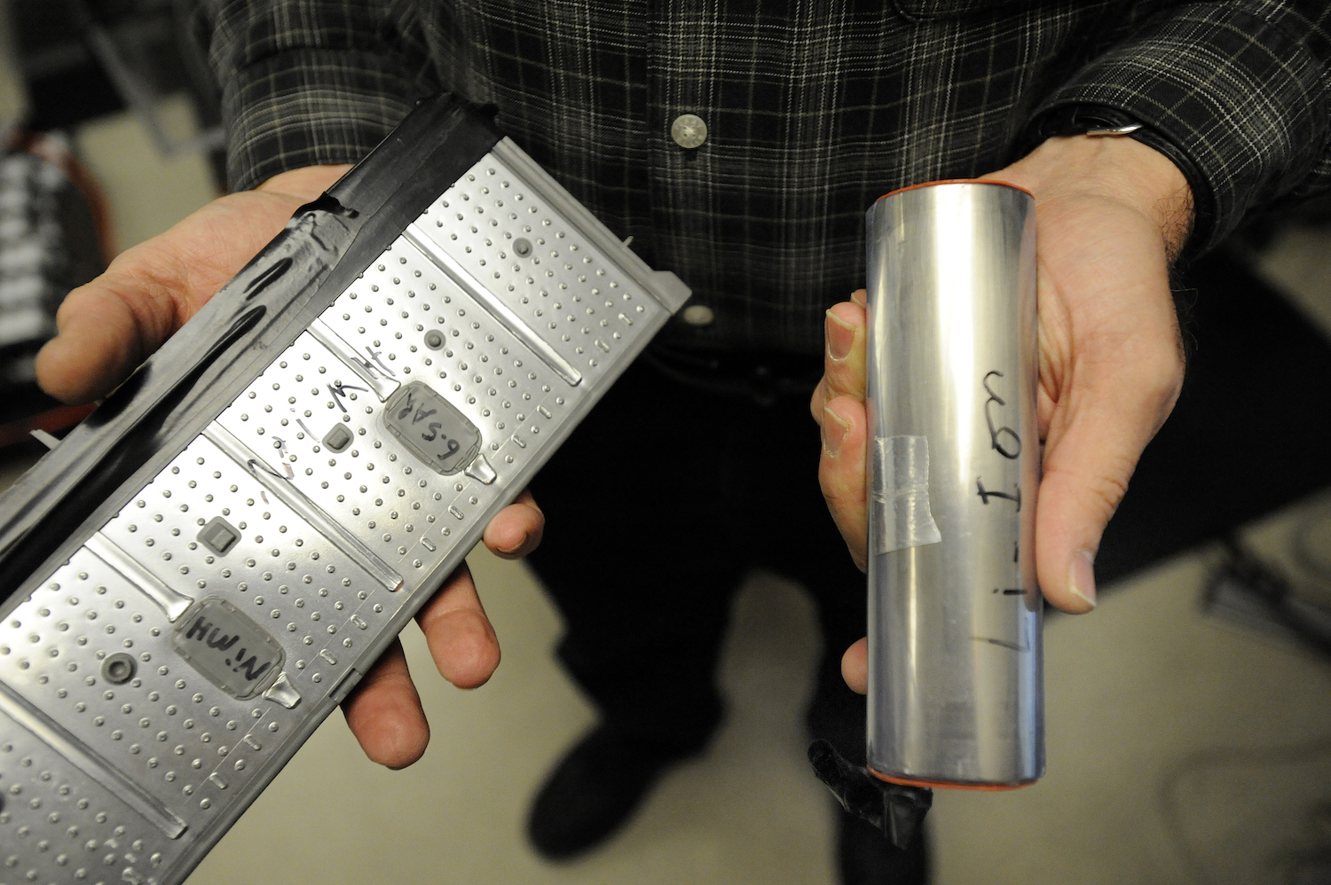 Closeup of a person's hands holding one cell of a Lithium-ion EV or hybrid battery and one cell of a Nickel Metal Hydride (NiMH) high-voltage traction battery.