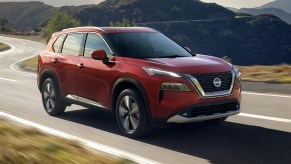 A red 2023 Nissan Rogue is driving on the road.