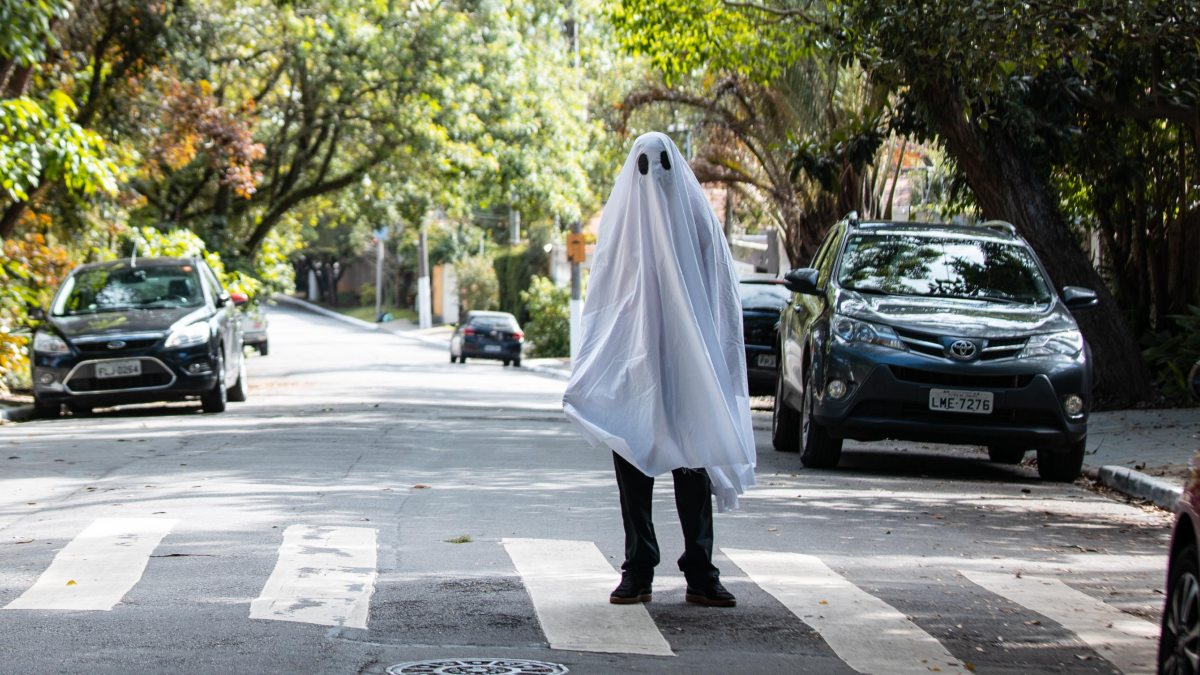 Person in ghost costume on street, highlighting if cars should be banned on Halloween, deadliest day for kids