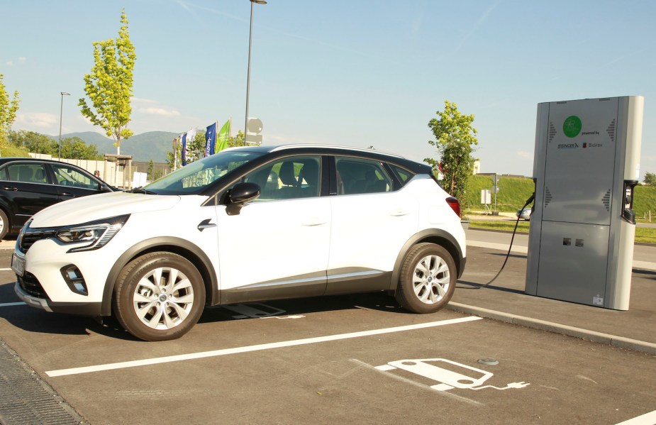 A Renault plug-in hybrid crossover SUV parked in a lot, a charger connected to its Li-ion battery.