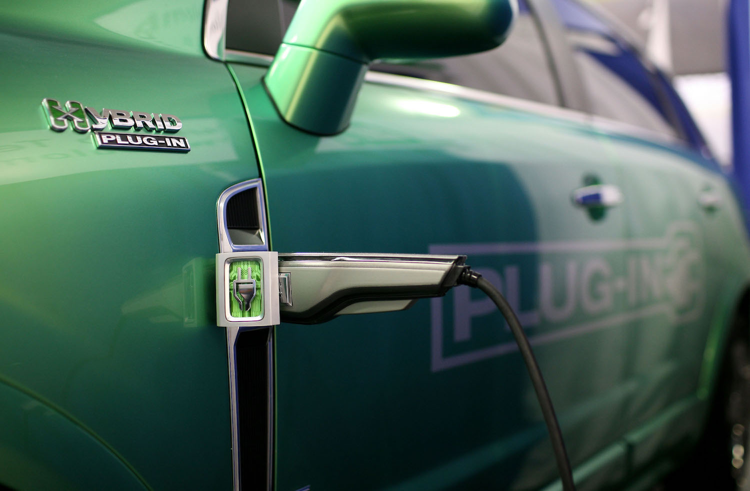 Close-up of a plug-in hybrid's charger in its green fender, PHEV badge visible in the foreground.