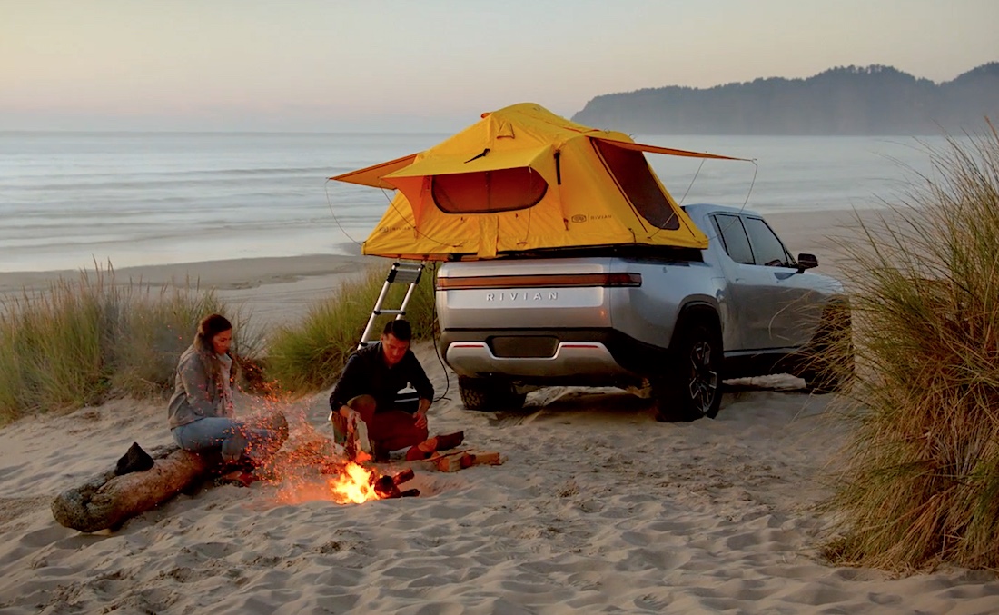 Promo photo of a couple camping next to a Rivian R1T electric pickup truck.