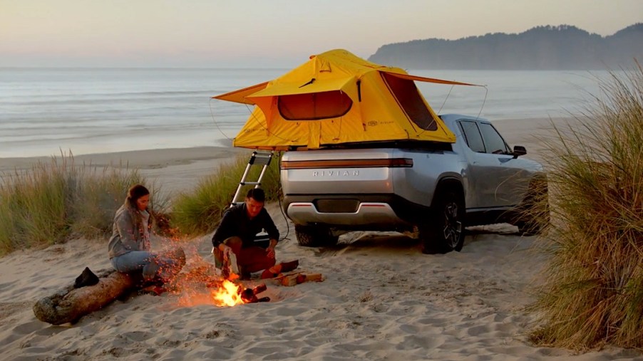 Promo photo of a couple camping next to a Rivian R1T electric pickup truck.