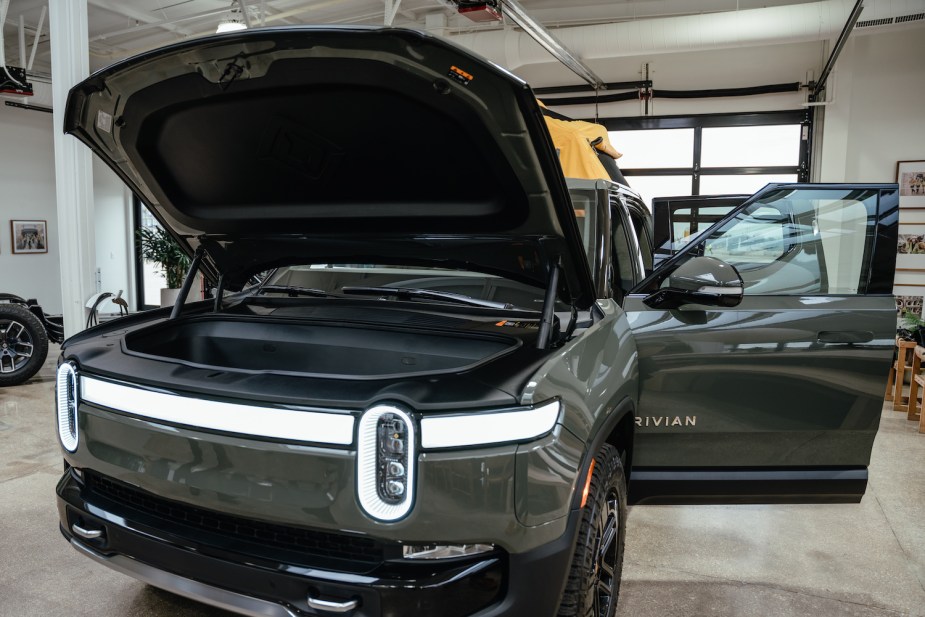 Dark green Rivian electric truck parked in a showroom with its doors and front trunk open.
