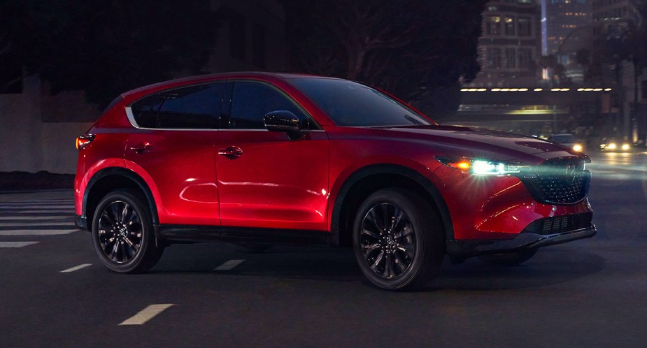 A red 2023 Mazda CX-5 small SUV is driving at night. 