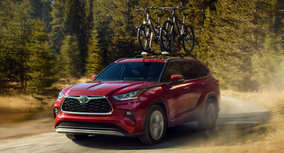 A red 2023 Toyota Highlander Hybrid is driving on the road. 