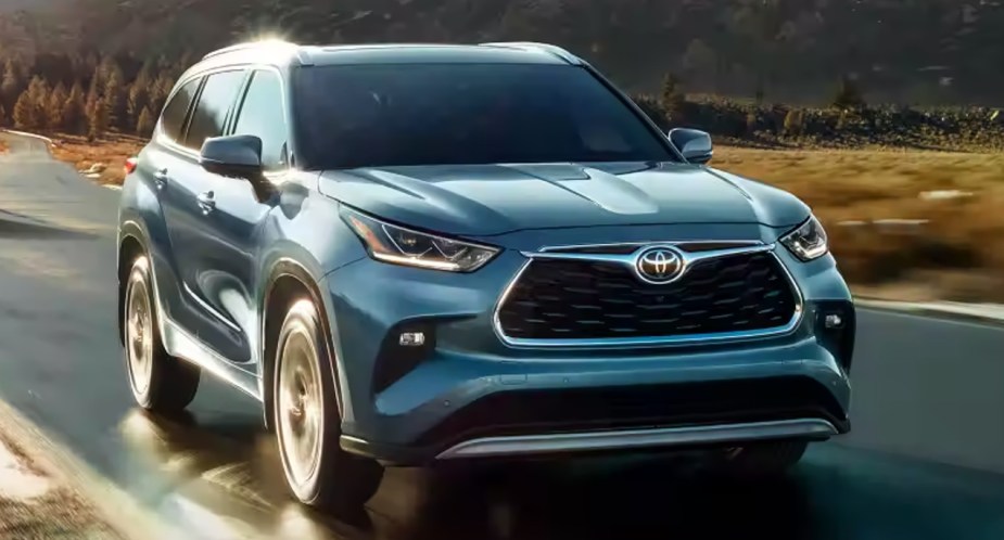 A blue Toyota Highlander Hybrid is driving on a damp road.