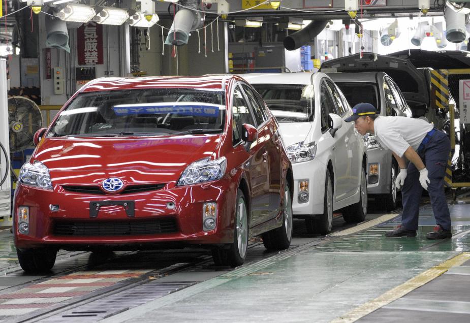 A technician looks at a row of Toyota Priuses in a factory.