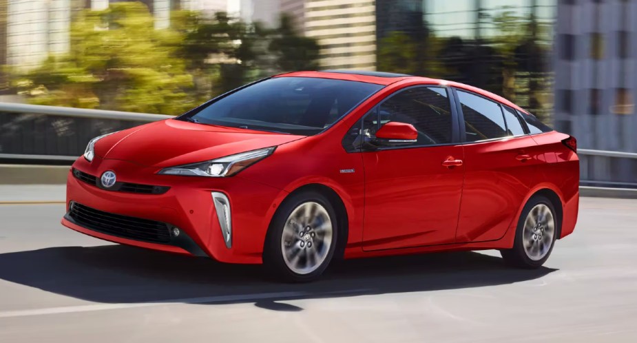 A red Toyota Prius is driving on the road. 