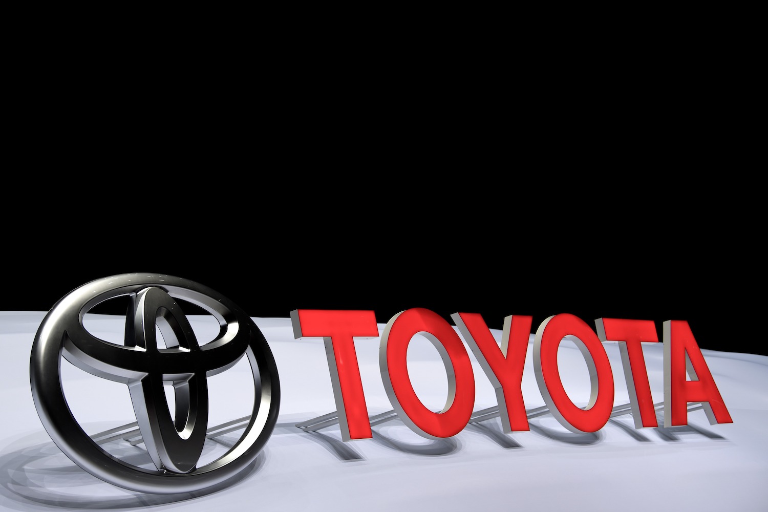 Toyota logo and the word Toyota on a white stage, with their shadows visible in the background.