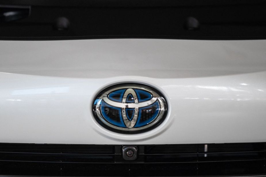 Closeup of the blue Toyota logo on the hood of a white Prius hybrid vehicle with a Lithium-ion battery.