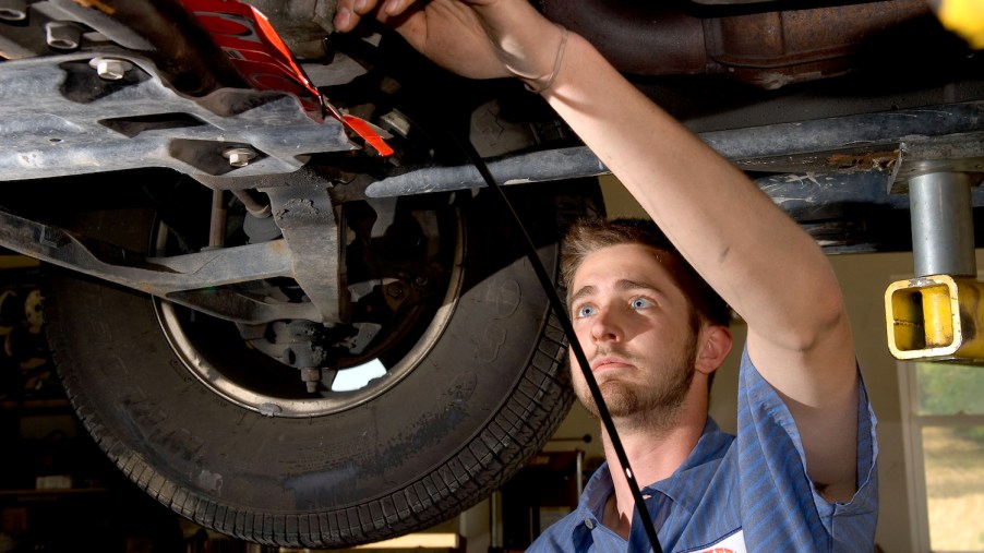 An auto technician maintains a vehicle on an overhead lift, one of its tires visible behind him.