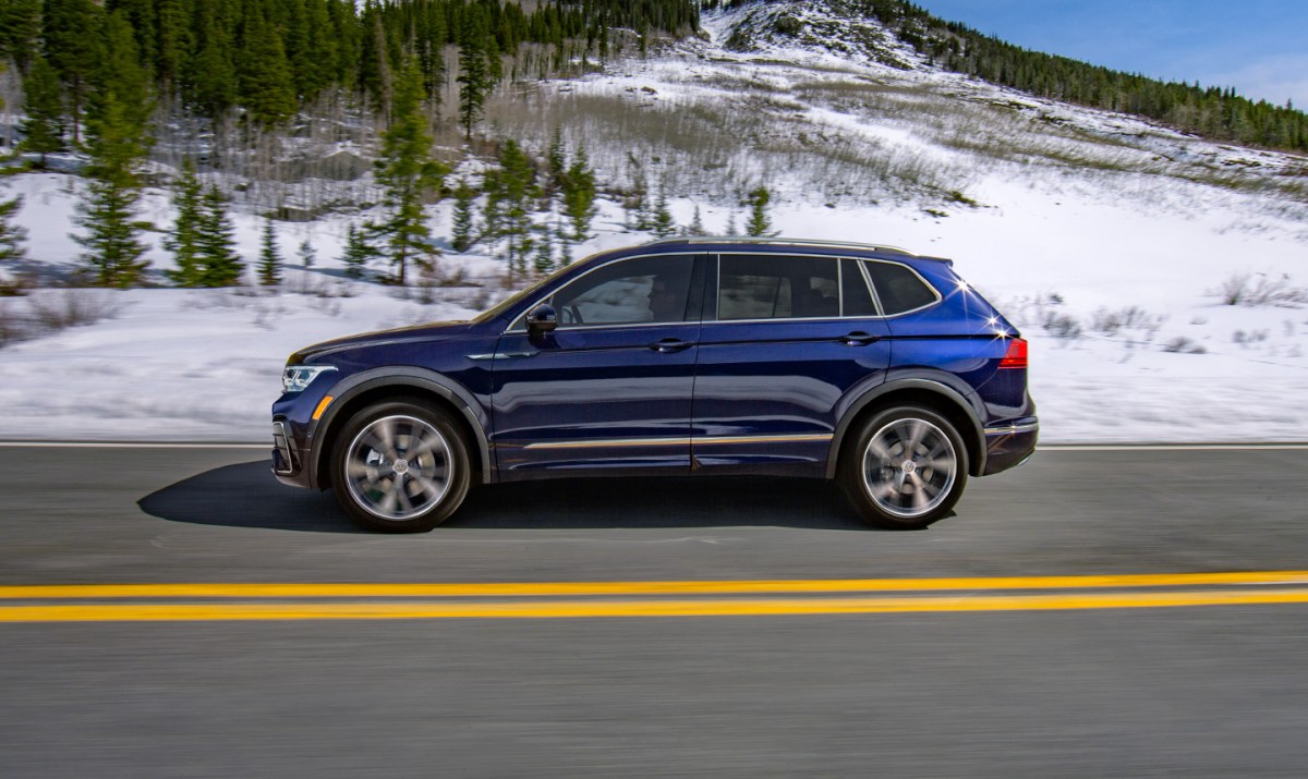 A blue 2022 Volkswagen Tiguan driving on a snowy road.  It is the cheapest three-row SUV.