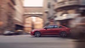 A red Volvo S60 driving on a historic city street.