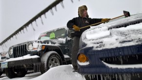 A car salesman brushes snow off of a car.