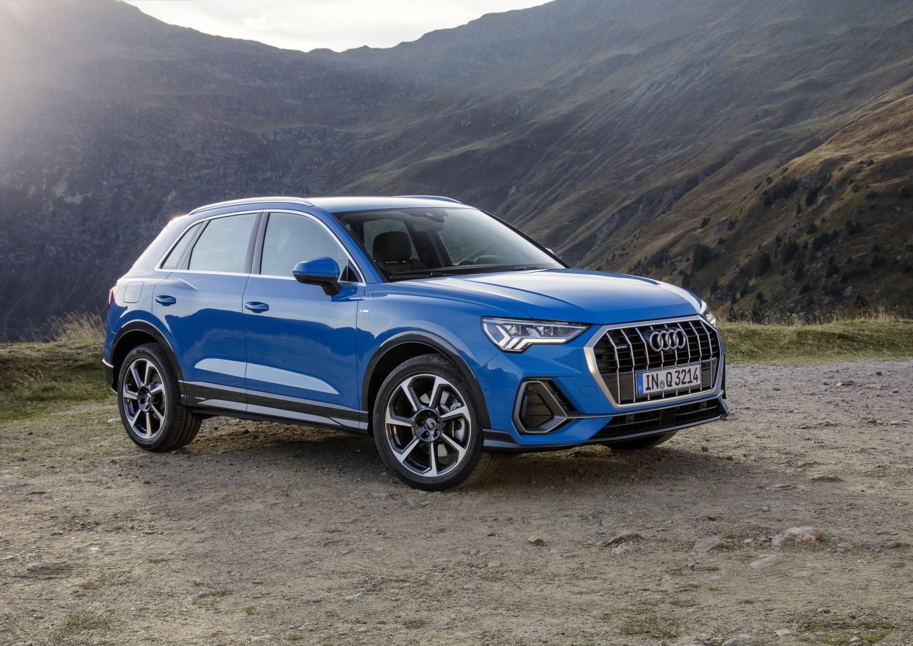 A blue Audi Q3 luxury subcompact SUV model parked on a plain of drip near mountains