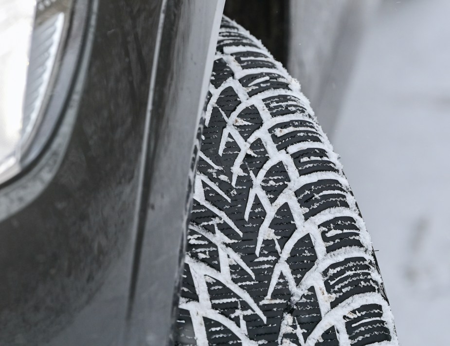 The tread of a winter tire on a car has been clogged by snow on the road.