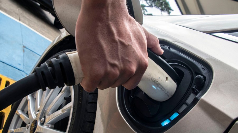 A person's hand connecting a high-speed electric charger to an electric vehicle's upgraded long range battery pack.
