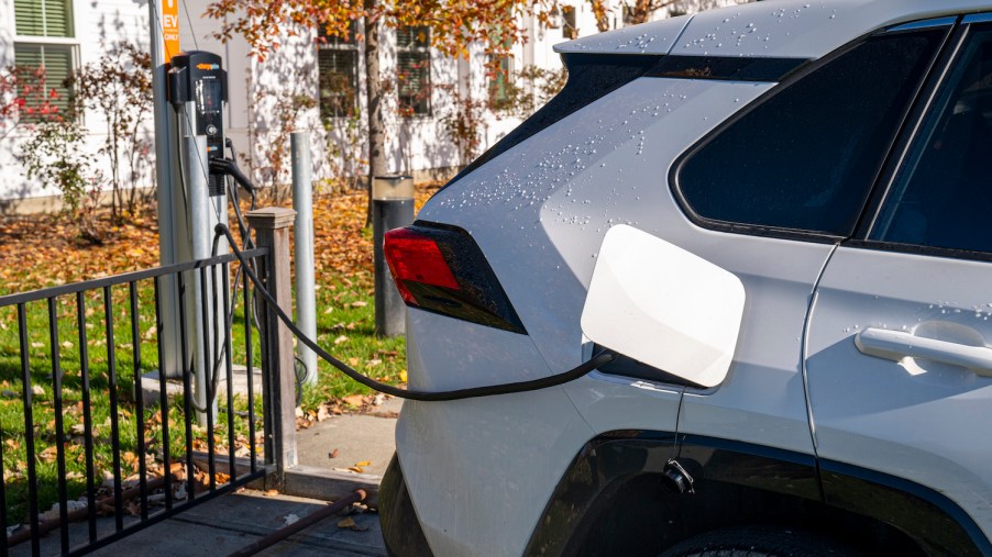 Closeup of a RAV4 Prime plug-in hybrid charging its battery, a Vermont lawn with fall foliage visible in the background.