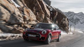 A red Mini John Cooper Works Clubman driving up a snowy mountain road near cliffs