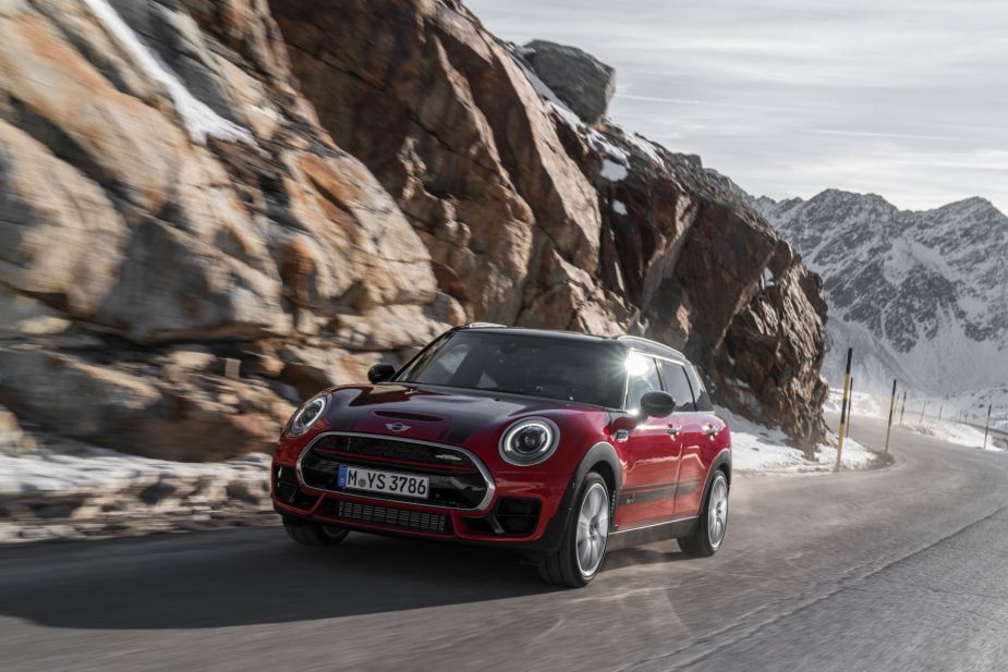 A red Mini John Cooper Works Clubman driving up a snowy mountain road near cliffs