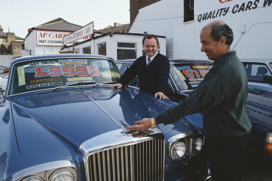 Second hand car salesman Vincent McCann admires a 1979 Bentley with a customer, UK, 1992.