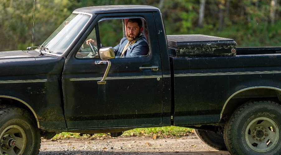 Automotive journalist Henry Cesari driving his classic square body Ford F-150 pickup truck, the woods of Vermont visible behind him.