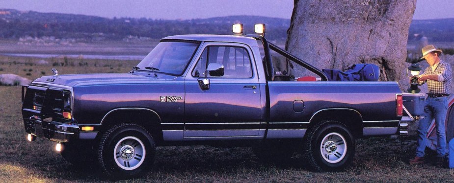 Advertising photo of a 4x4 square body Dodge Ram truck parked under a tree, a camper unloading a cooler and lantern from its tailgate.