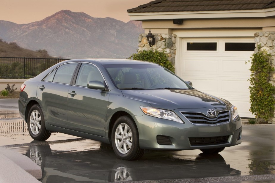 Green 2010 Toyota Camry midsize sedan parked in front of a house's garage, the sunsetting over a mountain range in the background.