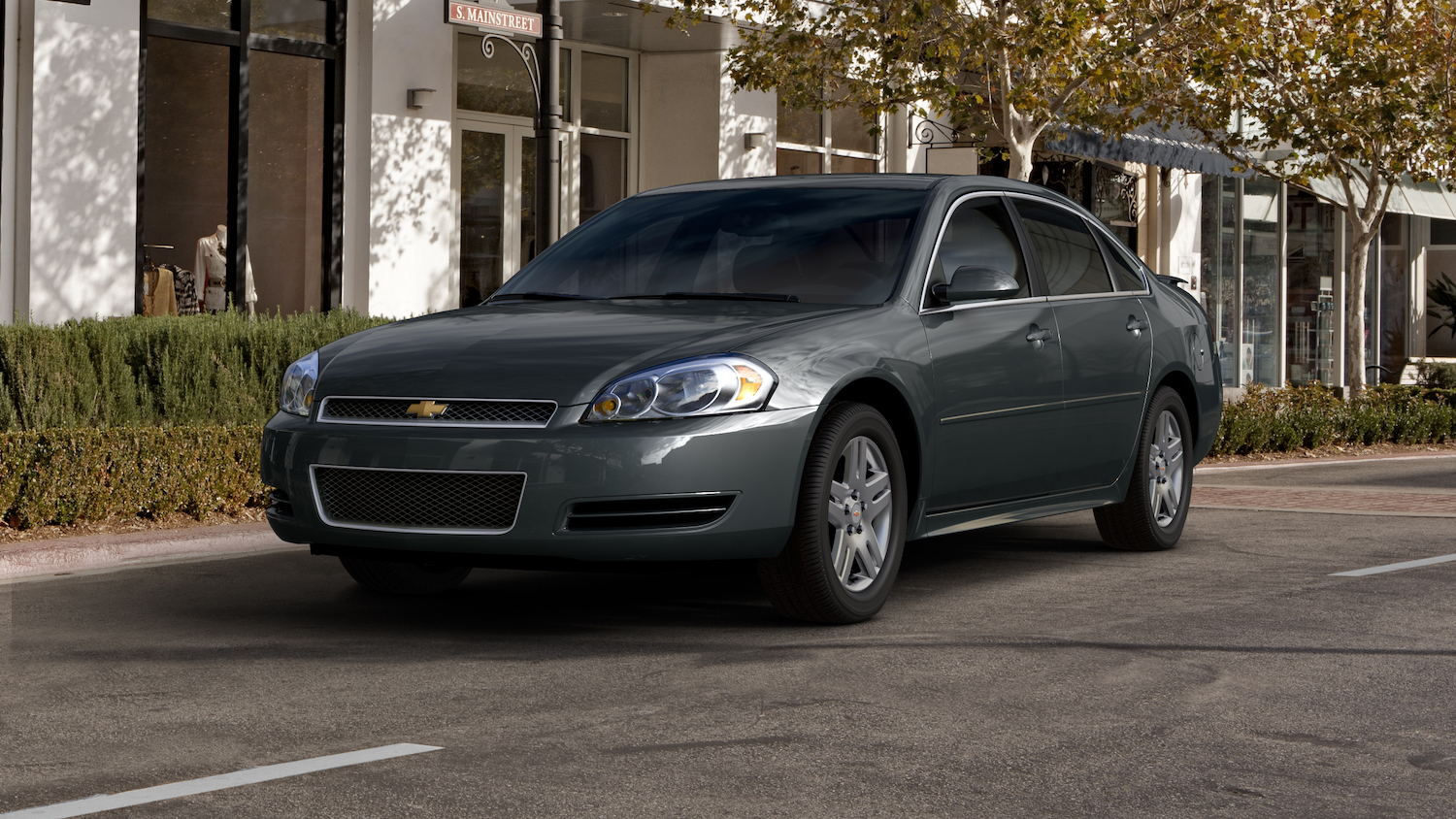 Dark gray Chevrolet Impala sedan parked on a tree-lined city street for a promo photo, a white building visible in the backgrond.