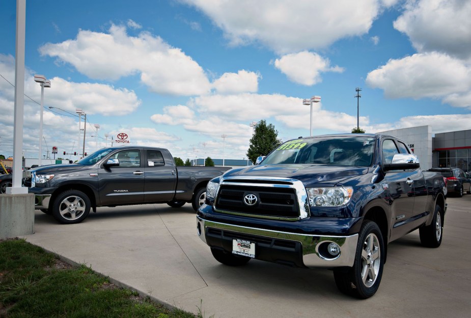 Two full-size Toyota Tundra pickup trucks parked in front of a Toyota dealership, a blue sky visible in the background.